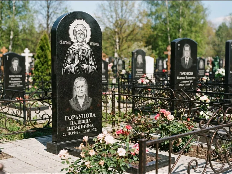 Памятник с гравировкой иконы: стела с арочным верхом и киотом под образ — гравировка образа Матроны Московской, гранитный цоколь с тёмной плиткой, работа «Ковалёв» в Оренбурге