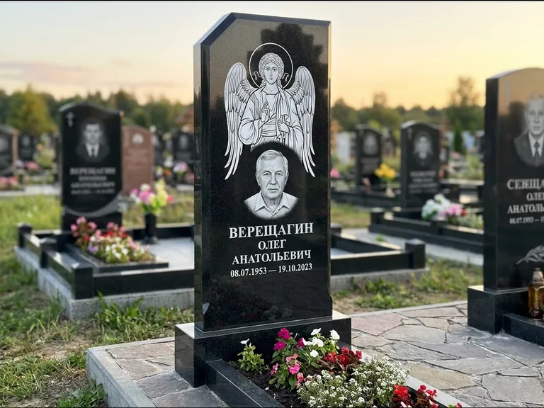 Памятник с гравировкой иконы: стела с резным навершием и нимбом в золоте — гравировка образа Спасителя, высокие разросшиеся туи полукругом, работа «Мельникова» в Оренбурге