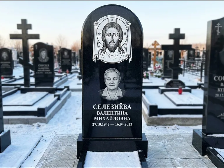 Памятник с гравировкой иконы: небольшая скромная одиночная стела с именной иконой — золочёный нимб на образе, аккуратный участок с газоном, работа «Ковалёв» в Оренбурге