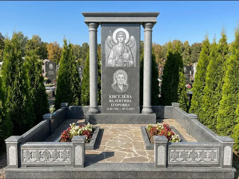 Памятник с гравировкой иконы: массивная стела с двускатным навершием-домиком — гравировка Николая Чудотворца, живая изгородь из туи, работа «Журавлёв» в Оренбурге