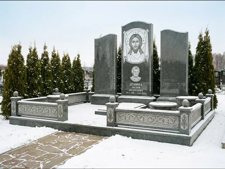Памятник с гравировкой иконы: узкая вертикальная стела-пилон с ликом — икона в резной рамке-киоте, открытая лужайка без ограды, работа «Одинцов» в Оренбурге