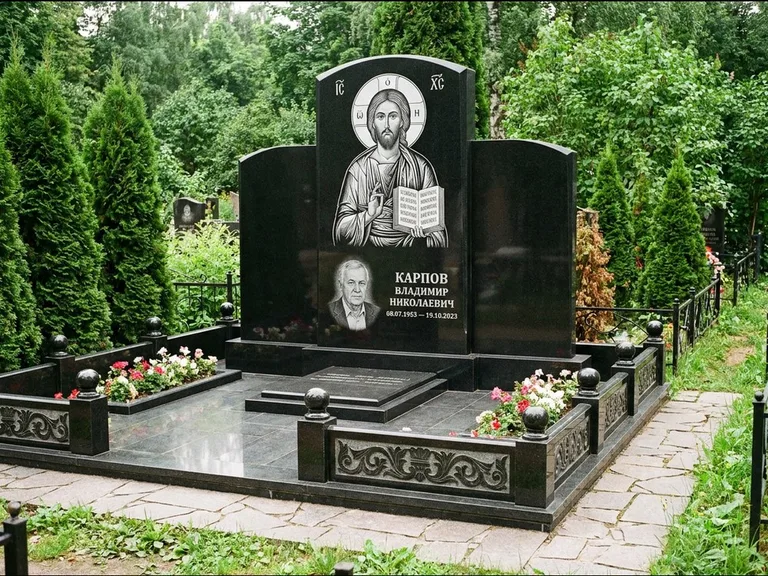 Памятник с гравировкой иконы: широкая панорамная стела с золочёным нимбом — гравировка образа Матроны Московской, цветник с белыми хризантемами, работа «Мельникова» в Оренбурге