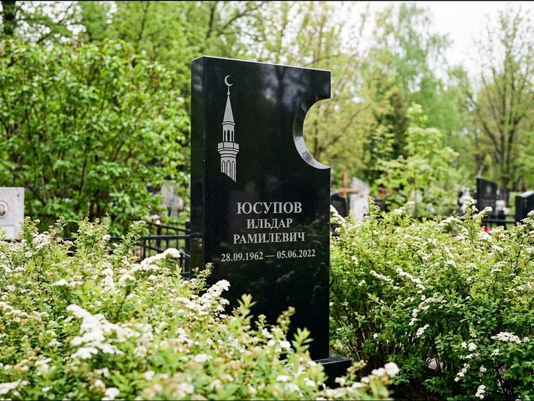 Мусульманский памятник с гравировкой мечети: стела с боковым вырезом в форме полумесяца — гравировка минарета с полумесяцем, низкие кусты спиреи в цвету, работа «Юсупов» в Оренбурге